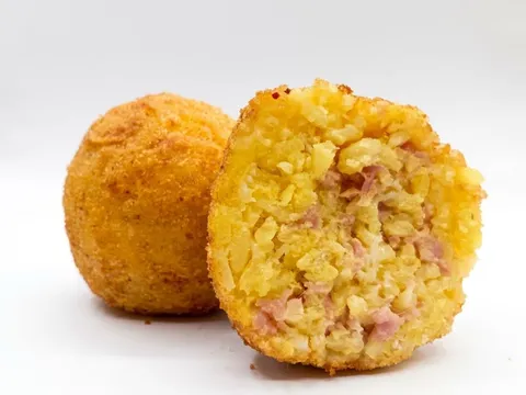 Arancino Cotto e Caciocavallo tagliato a metà, riso giallo con prosciutto cotto, accanto a un arancino intero dorato