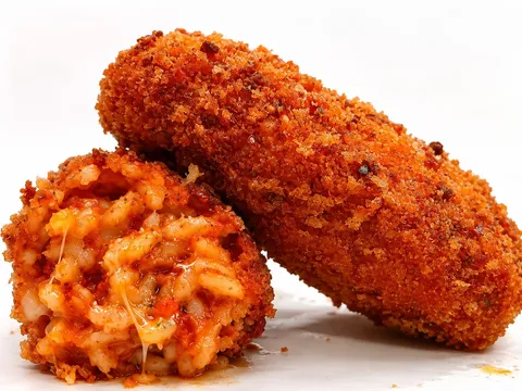 Supplì classico tagliato a metà, riso al pomodoro con filo di mozzarella, accanto a un supplì intero dorato